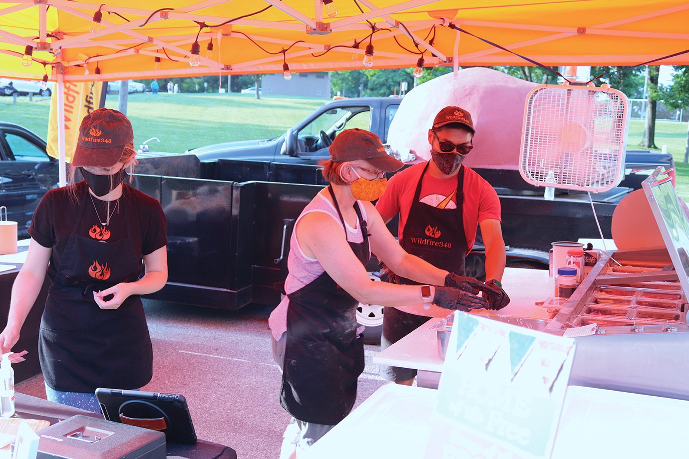 Though few food trucks and tents were available Saturday at Milligan Park, Wildfire 348 crew members Faith Galbert, from left, Kelly Green and Zach Green set up shop alongside Baldwin Memoral Field at Milligan Park ahead of Fourth of July celebrations.